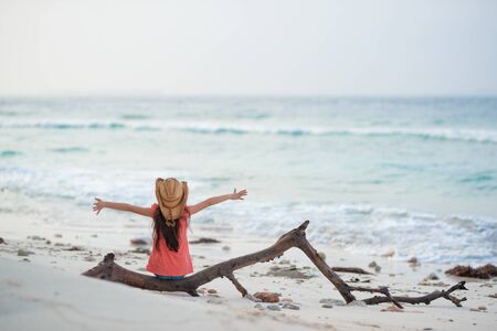 Girl sitting on driftwood on beachの写真素材