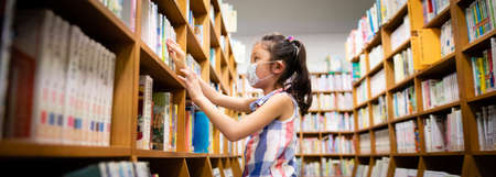 Girl wearing a mask choosing a book in the libraryの写真素材