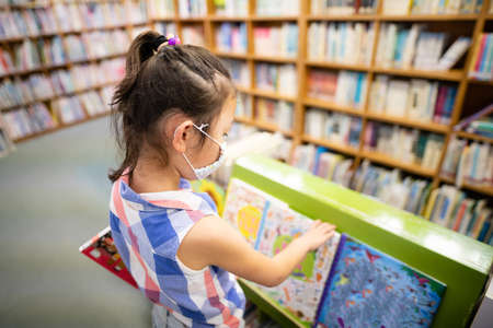 Girl wearing a mask choosing a book in the libraryの写真素材