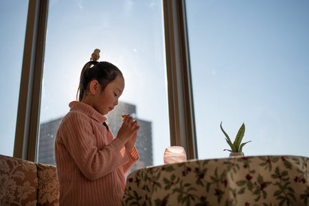 A girl eating a snack by the window of an apartmentの写真素材