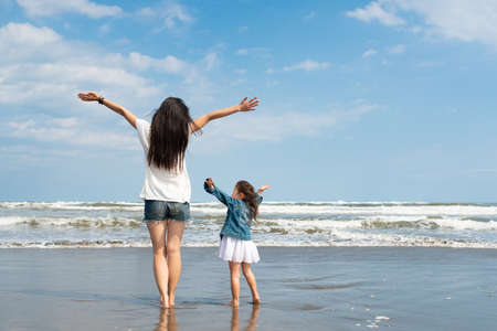 Mother and daughter spreading their hands on the beachの写真素材