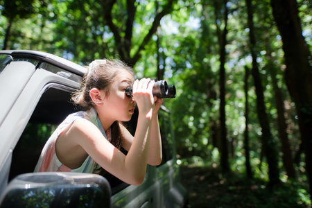 A child leaning out of a car window and using binoculars