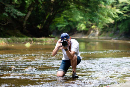 A man holding a single-lens reflex camera in a mountain streamの写真素材