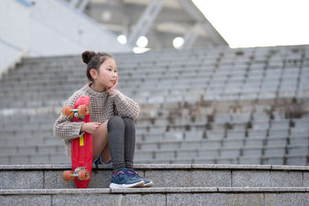 A girl with a skateboard sits on the stairsの写真素材