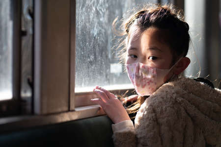 A girl wearing a mask and looking out the windowの写真素材