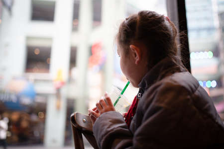 A girl drinking juice while looking out the windowの写真素材