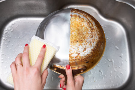 Woman's hand washing only half of a burnt frying panの写真素材