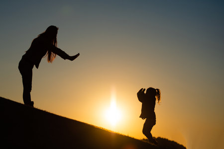 Mother and daughter playing in the meadow at sunsetの写真素材