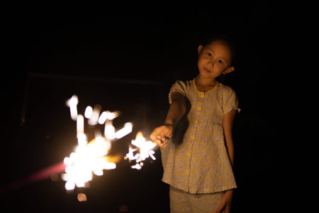 cute asian little girl holding sparklers on black background.
