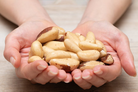 Woman hands holding a handful of pine nuts on a wooden background.