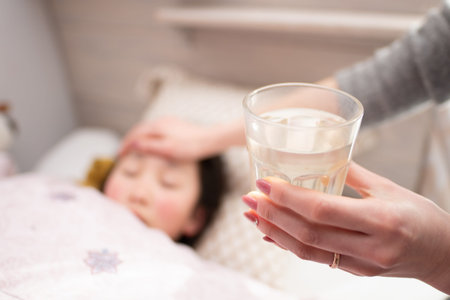 Mother giving glass of water to her daughter in bed. Focus on glass