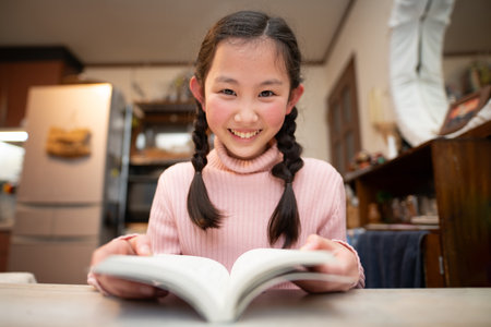 girl reading a book at the table in the kitchen.の写真素材