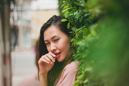 Woman standing leaning against a green leaf covering a wall.の写真素材