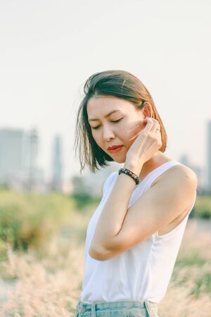 Woman standing in the grass field With hair that is swaying, the background has a sunset lightの写真素材