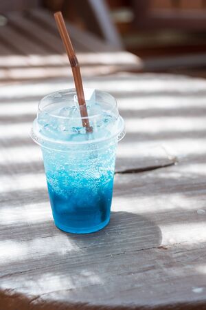 Blue soda in a plastic glass placed on a wooden tableの写真素材