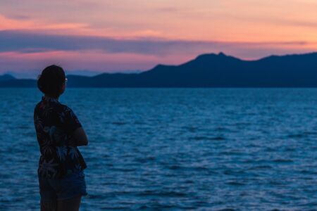 Silhouette of a woman standing with the sunset in the beautiful seaの写真素材