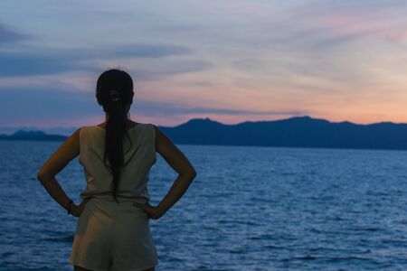 Silhouette of a woman standing with the sunset in the beautiful seaの写真素材
