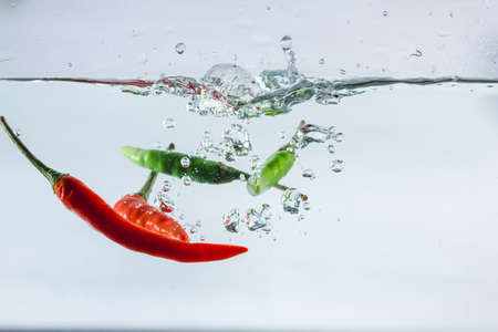 Red hot peppers fall into the splashing water.の写真素材