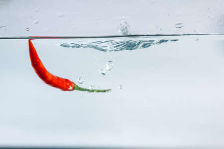 Red hot peppers fall into the splashing water.の写真素材