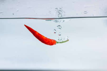 Red hot peppers fall into the splashing water.の写真素材