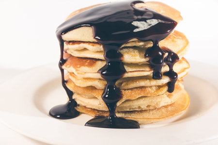 pancakes, stacked on a white plate, are topped with chocolate.の写真素材