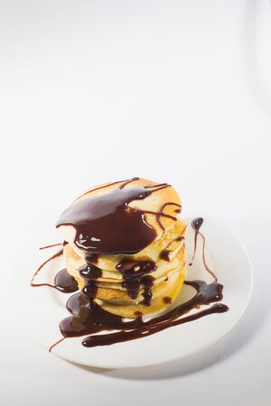 pancakes, stacked on a white plate, are topped with chocolate.の写真素材
