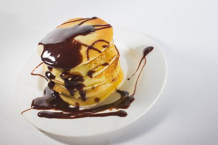pancakes, stacked on a white plate, are topped with chocolate.の写真素材