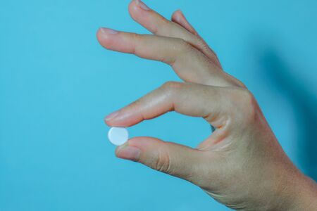 Medication on hand,
White seed medicine on fingers, on a blue backgroundの写真素材