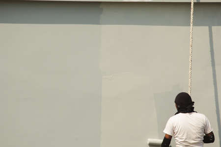 A male worker is painting a tall building abseiling.の写真素材