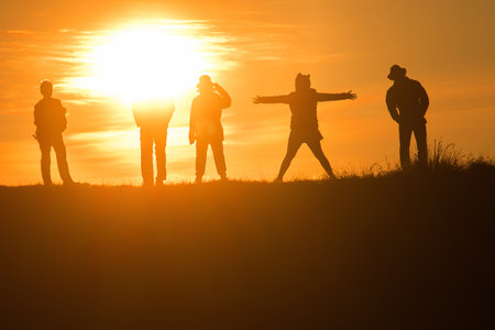 Travelers silhouettes against the orange light of sunset on the mountains.の写真素材