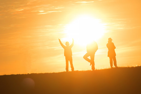 Travelers silhouettes against the orange light of sunset on the mountains.の写真素材