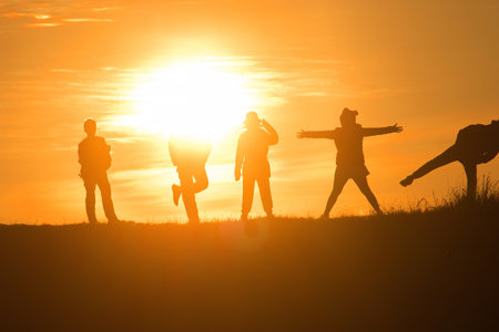 Travelers silhouettes against the orange light of sunset on the mountains.の写真素材