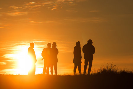 Travelers silhouettes against the orange light of sunset on the mountains.の写真素材