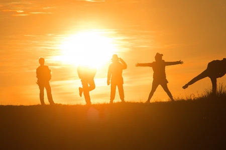 Travelers silhouettes against the orange light of sunset on the mountains.の写真素材