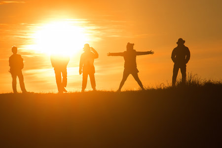 Travelers silhouettes against the orange light of sunset on the mountains.の写真素材