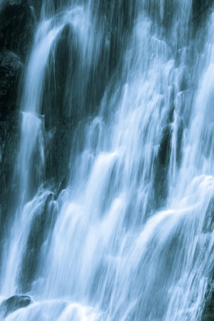 The water flows down from the rock cliff. It hits the cliff and creates mist.の写真素材