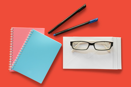 Letter envelope, eye glasses, pens and note books isolated on red backgroundの写真素材