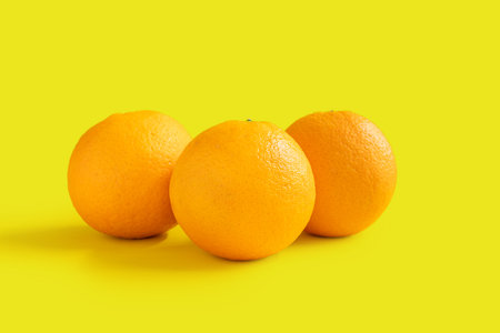 Photo of three navel oranges isolated on yellow background
