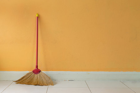 A grass broom  lean against the orange wall