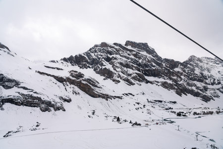 A photo of a snow-covered mountain peak in winter, with a cable car line visible on the right side of the image.の写真素材