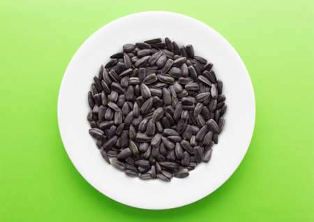 White round plate with black roasted sunflower seeds on green background.の写真素材