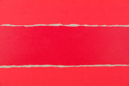Torn piece of red cardboard on red paper background. Stripe of red cardboard with copy space for...