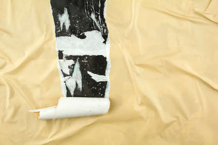 Torn and peeling beige poster glued on billboard with old dirty paper. Abstract and creative background of ripped beige glossy magazine paper.の写真素材