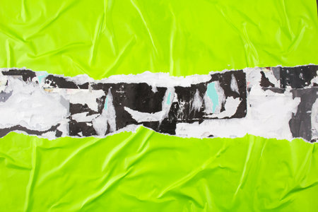 Crumpled and torn green paper poster glued on billboard. Abstract and creative background of ripped green glossy magazine paper.の写真素材