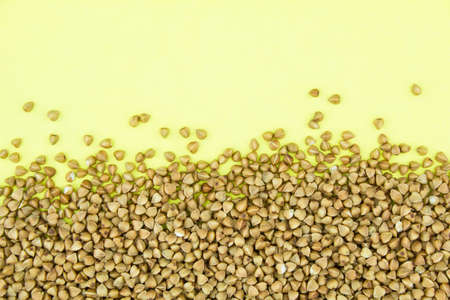 Brown raw buckwheat grains on yellow paper background. Copy space for text.の写真素材