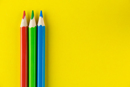 Red, green and blue pencils on yellow background. Copy space for text.