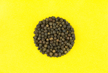 Black pepper on yellow background. Heap of black peppercorns.