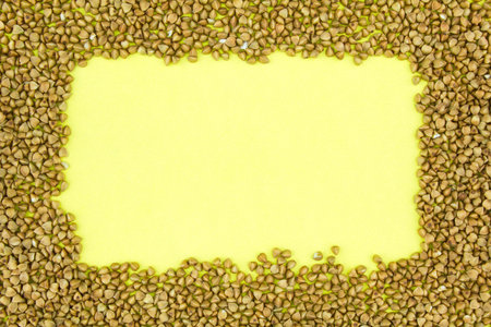 Frame from brown buckwheat grains on yellow paper background. Copy space for text.
