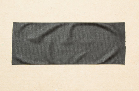 Black piece of matte cloth adheisive gaffer tape on brown cardboard background. Copy space for text.