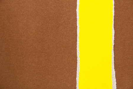 Yellow torn piece of cardboard on brown sheet of paper texture background. Can be used for text.の写真素材